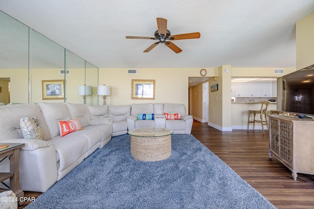 living area featuring dark wood finished floors, visible vents, a ceiling fan, a textured ceiling, and baseboards