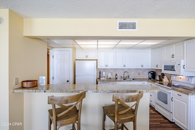 kitchen featuring white appliances, visible vents, white cabinets, a breakfast bar, and a sink