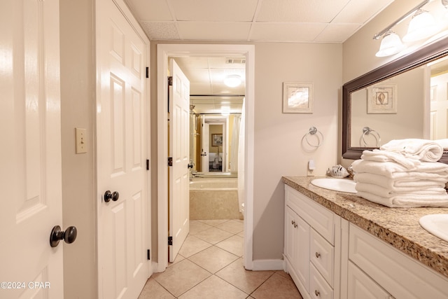 full bath with a drop ceiling, tile patterned flooring, a sink, baseboards, and double vanity