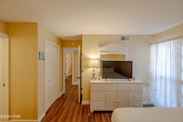 bedroom with baseboards, visible vents, dark wood finished floors, and a textured ceiling