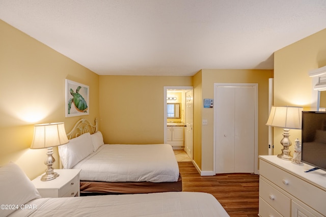 bedroom with ensuite bath, wood finished floors, and baseboards