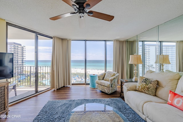 living area featuring a textured ceiling, a view of the beach, a water view, wood finished floors, and floor to ceiling windows