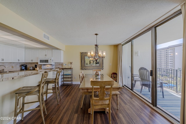 dining space with dark wood-style floors, a notable chandelier, visible vents, expansive windows, and a textured ceiling