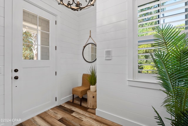 entrance foyer with light wood-type flooring, wood walls, and an inviting chandelier