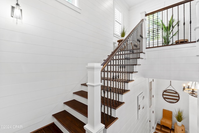 staircase with an inviting chandelier, wood walls, and hardwood / wood-style flooring