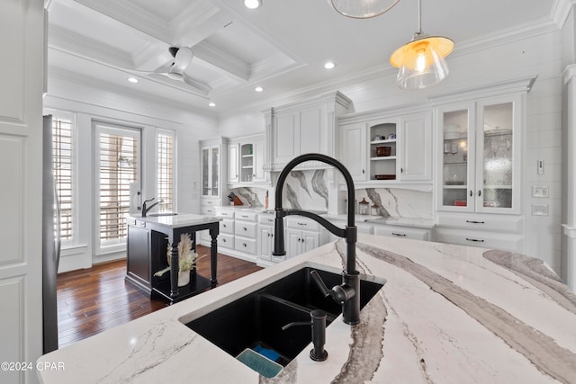 kitchen with coffered ceiling, light stone counters, white cabinets, ceiling fan, and sink