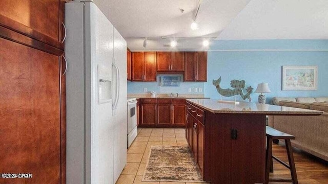 kitchen featuring a kitchen island, a kitchen breakfast bar, light tile patterned floors, white appliances, and a textured ceiling