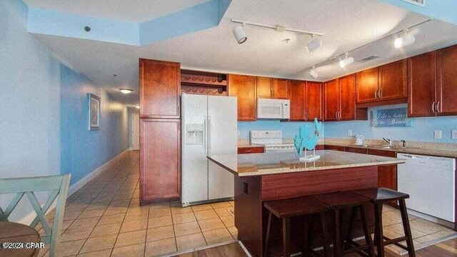 kitchen with light tile patterned flooring, a kitchen breakfast bar, a center island, white appliances, and track lighting