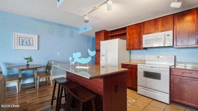 kitchen featuring a breakfast bar, a center island, light tile patterned floors, track lighting, and white appliances