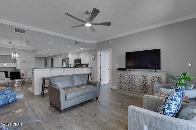 living room with a textured ceiling, ceiling fan with notable chandelier, light hardwood / wood-style floors, and crown molding