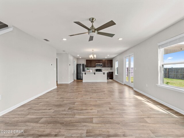 unfurnished living room featuring ceiling fan with notable chandelier and light hardwood / wood-style flooring