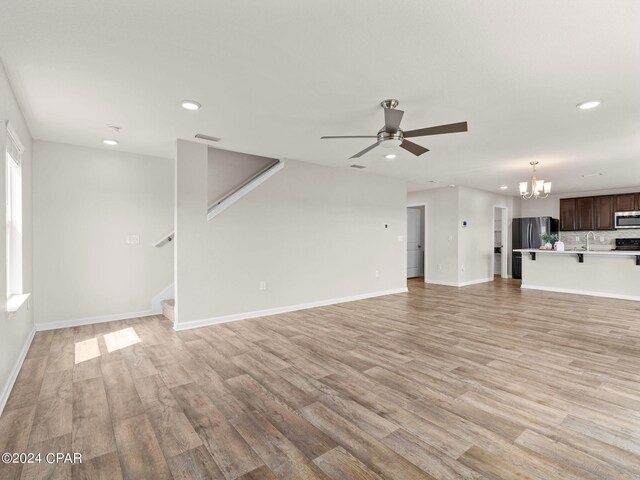 unfurnished living room featuring ceiling fan with notable chandelier and light hardwood / wood-style flooring