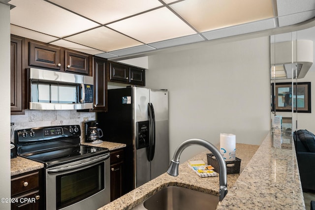 kitchen with a drop ceiling, light stone counters, and stainless steel appliances