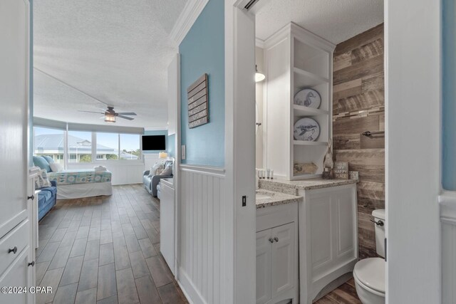 bathroom with wood walls, vanity, a textured ceiling, ceiling fan, and toilet