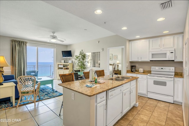 kitchen featuring white cabinetry, white appliances, a center island with sink, light stone countertops, and ceiling fan