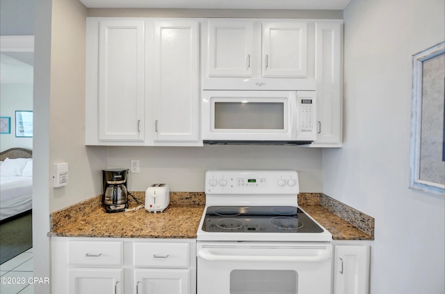 kitchen with dark stone counters, white appliances, and white cabinetry