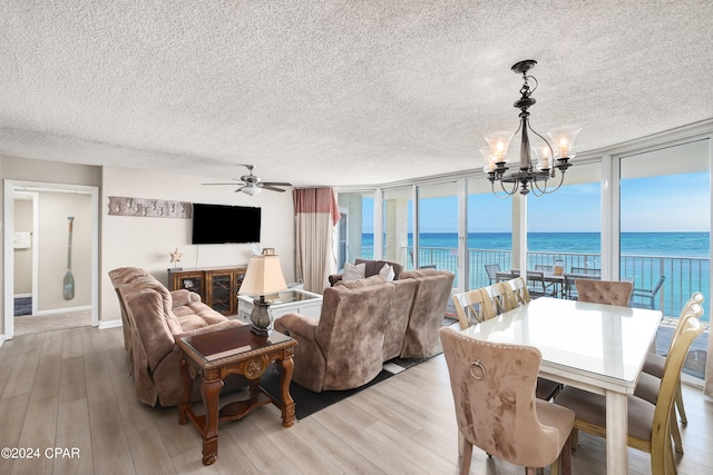 living room featuring a wall of windows, ceiling fan with notable chandelier, a textured ceiling, and light wood-type flooring