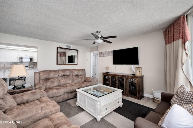 living room with ceiling fan, a textured ceiling, and light wood-type flooring