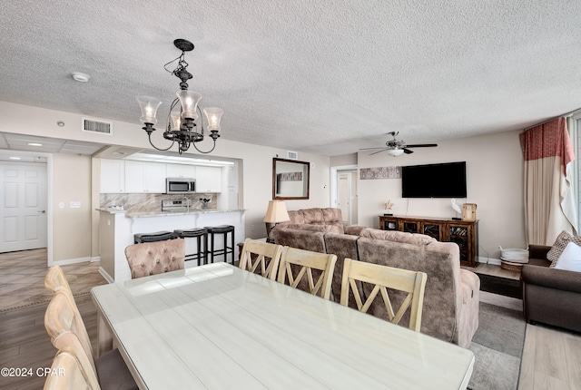 dining space with a textured ceiling, ceiling fan with notable chandelier, and light hardwood / wood-style flooring