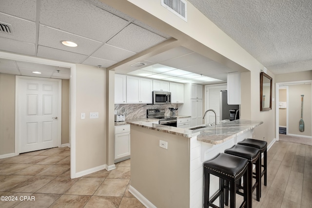 kitchen featuring kitchen peninsula, white cabinetry, stainless steel appliances, light stone countertops, and a kitchen bar