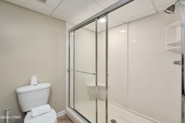 bathroom featuring a drop ceiling, a shower with shower door, and toilet