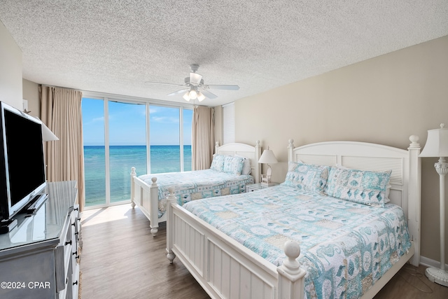 bedroom with access to outside, ceiling fan, wood-type flooring, a textured ceiling, and a water view