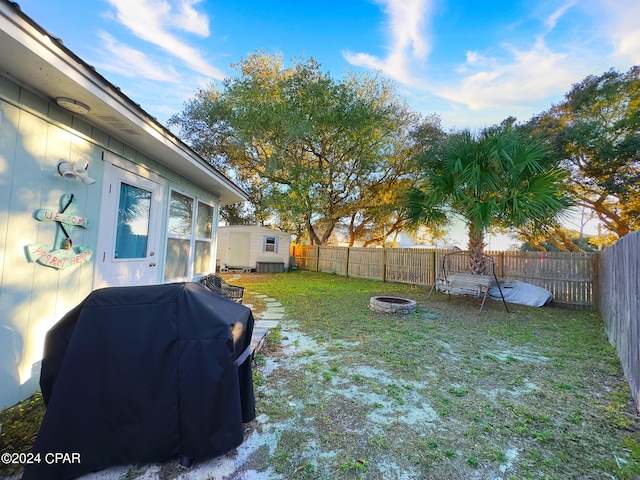 view of yard featuring an outbuilding, a storage unit, a fenced backyard, and an outdoor fire pit