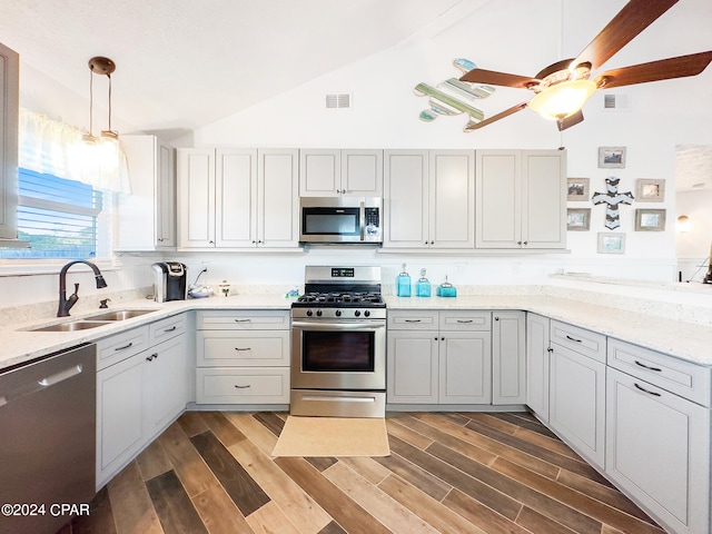 kitchen with appliances with stainless steel finishes, vaulted ceiling, decorative light fixtures, hardwood / wood-style floors, and sink