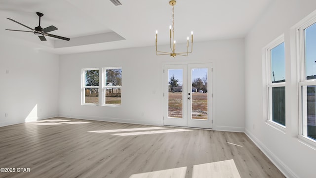 unfurnished room featuring french doors, an inviting chandelier, a raised ceiling, and light hardwood / wood-style floors