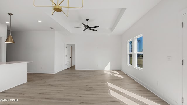 unfurnished living room featuring ceiling fan, light wood-type flooring, and a tray ceiling