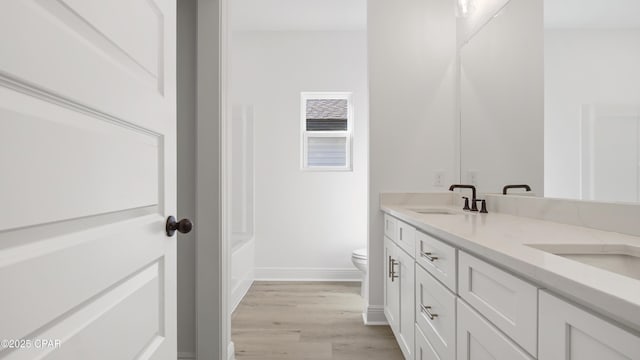 bathroom featuring wood-type flooring, a bath, vanity, and toilet