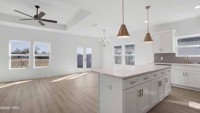 kitchen with a raised ceiling, white cabinetry, a kitchen island, and pendant lighting