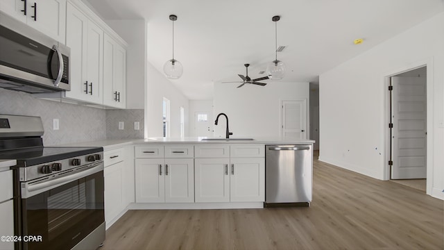 kitchen featuring light wood-style flooring, a peninsula, a sink, white cabinetry, and appliances with stainless steel finishes