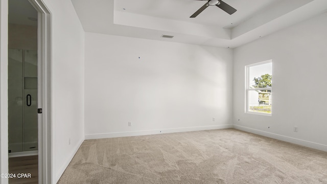 carpeted spare room with a tray ceiling, visible vents, ceiling fan, and baseboards