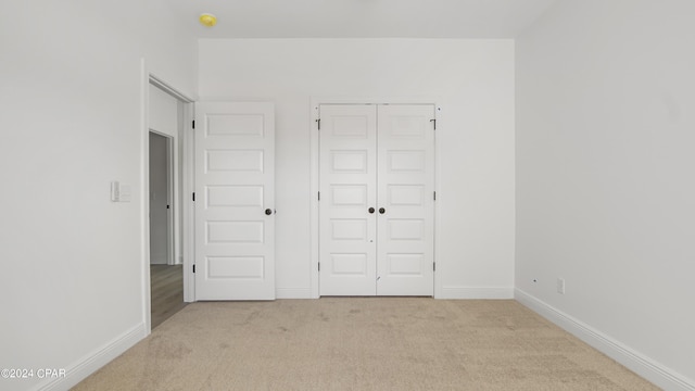 unfurnished bedroom featuring light carpet, a closet, and baseboards