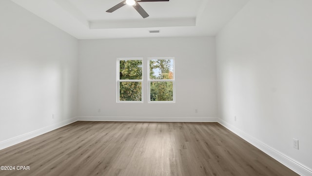 empty room featuring a tray ceiling, ceiling fan, and light hardwood / wood-style floors