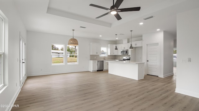 kitchen with appliances with stainless steel finishes, light wood-type flooring, decorative light fixtures, white cabinets, and a center island