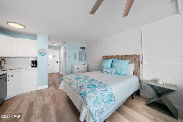 bedroom with a textured ceiling, light hardwood / wood-style flooring, wood walls, and sink