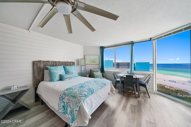 bedroom with a beach view, hardwood / wood-style floors, a water view, ceiling fan, and a textured ceiling