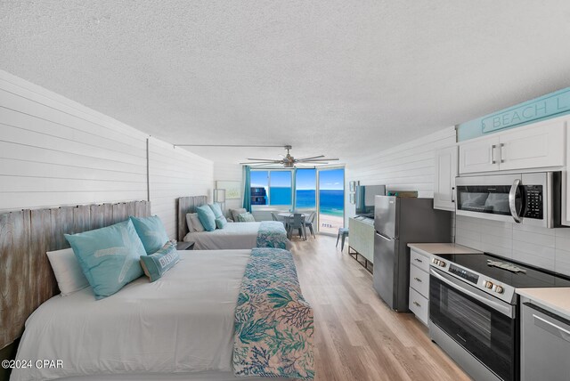 bedroom with a textured ceiling, ceiling fan, stainless steel refrigerator, and light wood-type flooring