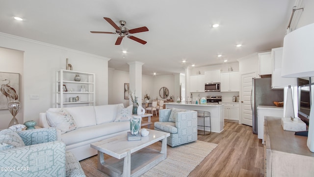 living room with ornate columns, ceiling fan, crown molding, sink, and light hardwood / wood-style flooring