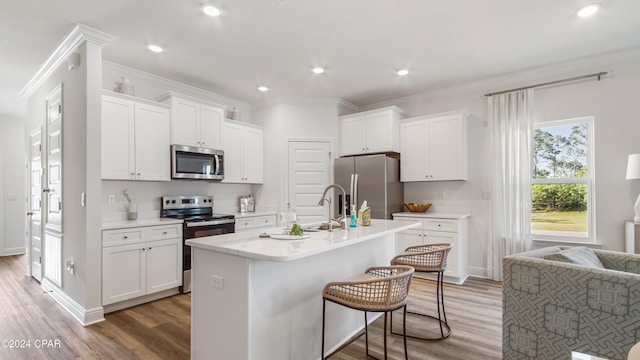 kitchen featuring white cabinetry, hardwood / wood-style flooring, a kitchen island with sink, appliances with stainless steel finishes, and ornamental molding