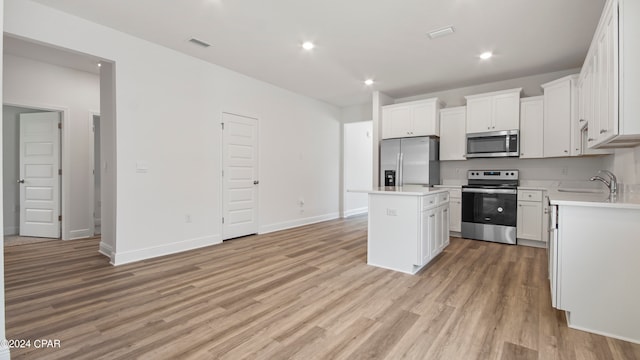 kitchen with a center island, stainless steel appliances, sink, white cabinets, and light hardwood / wood-style flooring