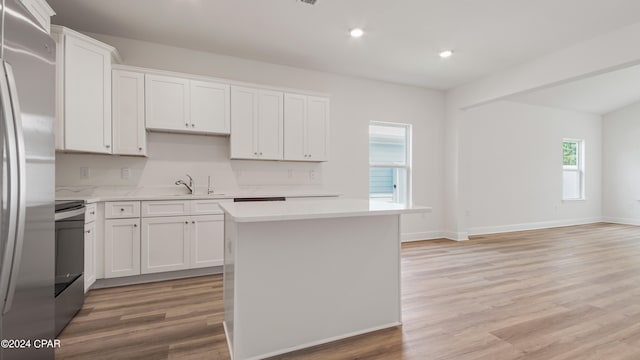 kitchen with light hardwood / wood-style floors, a center island, white cabinets, sink, and appliances with stainless steel finishes