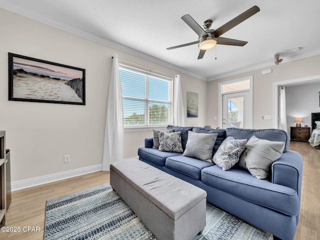 living area with light wood-style floors, baseboards, ornamental molding, and a ceiling fan