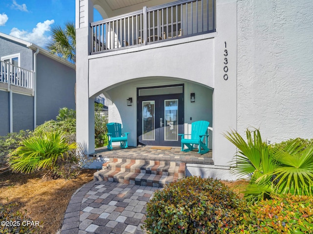 entrance to property featuring french doors, a balcony, and stucco siding