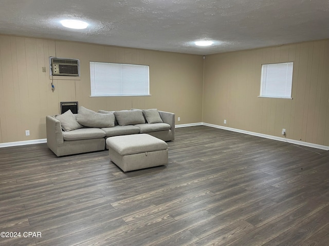 living room featuring dark wood-type flooring, a wall unit AC, and a textured ceiling