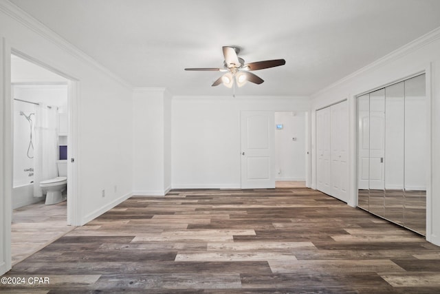 unfurnished bedroom with dark hardwood / wood-style floors, multiple closets, ensuite bathroom, ceiling fan, and crown molding