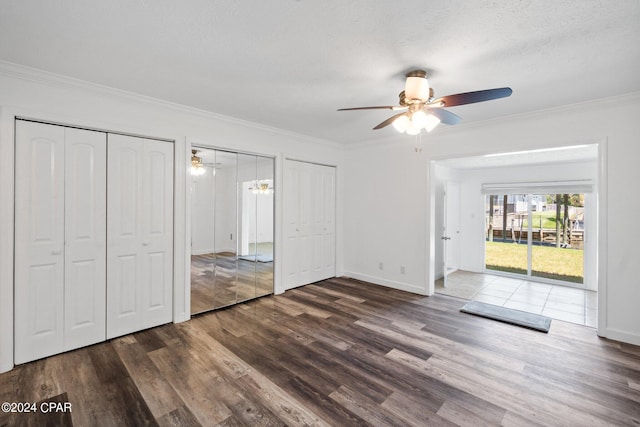 unfurnished bedroom featuring dark wood-type flooring, multiple closets, access to outside, a textured ceiling, and ceiling fan