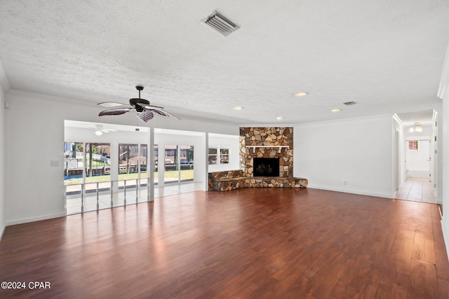 unfurnished living room featuring ceiling fan, a stone fireplace, ornamental molding, dark tile patterned flooring, and a textured ceiling